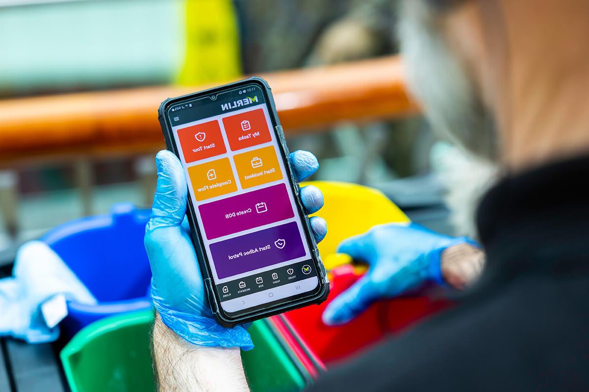 A person wearing blue plastic gloves, holding a smartphone device to use Merlin software